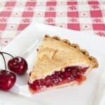 slice-of-cherry-pie-with-cherry-on-side-on-plate-169960522-67fcb3cdc8024ea48f2f5a8cd3d2fd8c